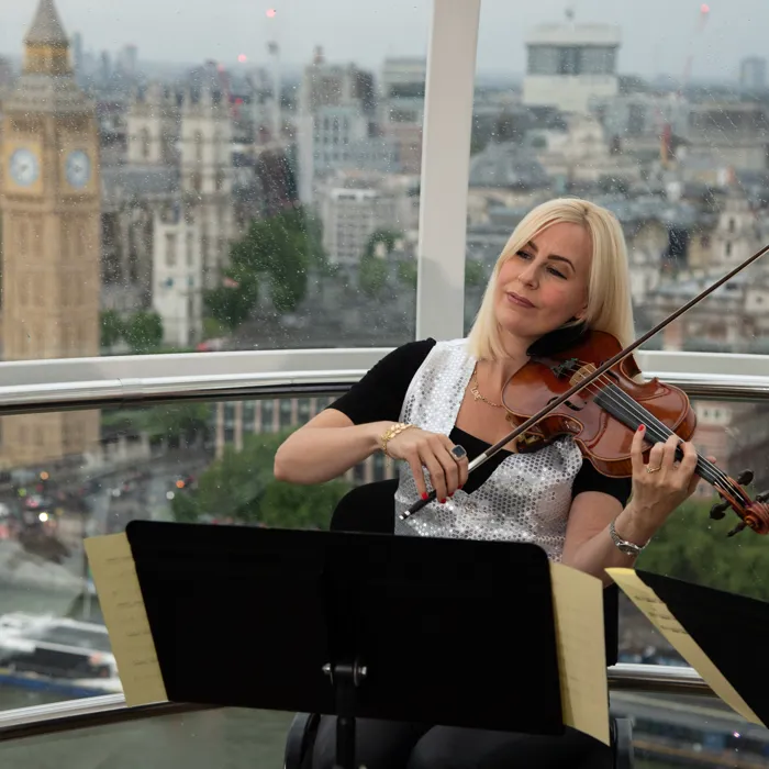 Violinist performing inside a London Eye Pod with Big Ben visible in the distance.